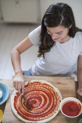 Junge Frau, die Tomatensauce auf Pizzateig verteilt - RIBF000199