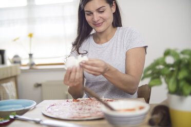 Junge Frau, die Mozzarella-Käse auf eine Pizza legt - RIBF000201