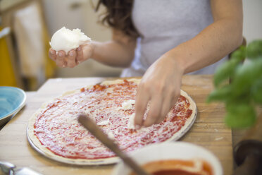 Junge Frau, die Mozzarella-Käse auf eine Pizza legt - RIBF000202