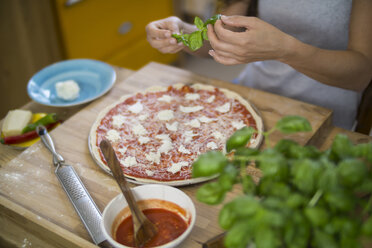 Junge Frau bei der Zubereitung einer Pizza mit Mozzarella, Chilischoten und Basilikum - RIBF000203