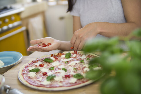 Junge Frau bei der Zubereitung einer Pizza mit Mozzarella, Chilischoten und Basilikum - RIBF000204