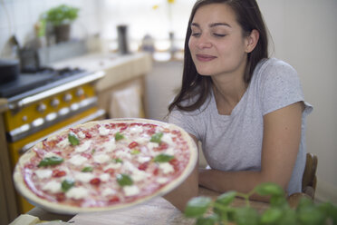 Junge Frau mit selbstgemachter Pizza mit Mozzarella, Chilischoten und Basilikum - RIBF000206