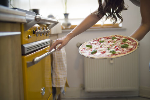 Junge Frau mit selbstgemachter Pizza mit Mozzarella, Chilischoten und Basilikum - RIBF000207