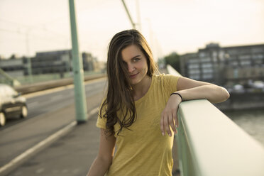 Germany, Cologne, portrait of young woman standing on Rhine bridge at evening twilight - RIBF000218