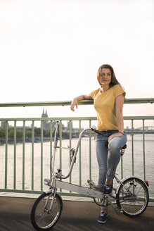 Germany, Cologne, young woman with bicycle standing on Rhine bridge - RIBF000222