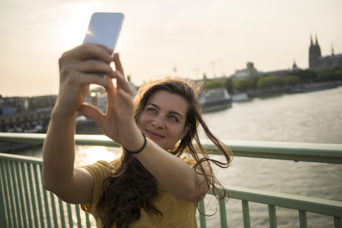 Germany, Cologne, young woman standing on Rhine bridge taking a selfie with her smartphone stock photo