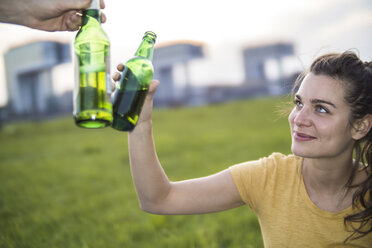 Deutschland, Köln, Frau stößt mit Bierflasche auf einer Wiese in der Abenddämmerung an - RIBF000246