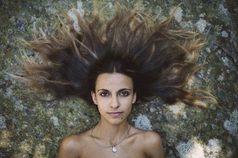 Porträt einer auf einem Felsen liegenden Frau mit zerzaustem Haar, lizenzfreies Stockfoto