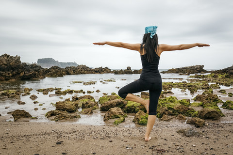 Spanien, Asturien, Gijon, Frau beim Yoga an einem Felsstrand, lizenzfreies Stockfoto