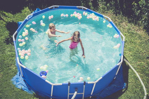 Junge und Mädchen im Schwimmbad, umgeben von Luftballons, lizenzfreies Stockfoto