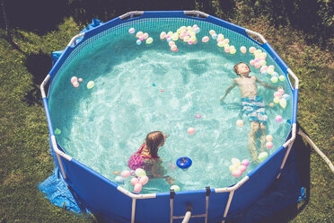 Boy and girl in swimming pool surrounded by balloons - SARF002067