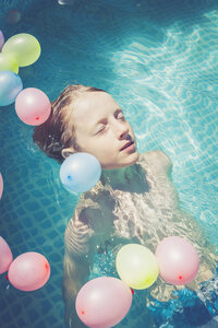 Junge im Schwimmbad, umgeben von im Wasser schwimmenden Luftballons - SARF002068