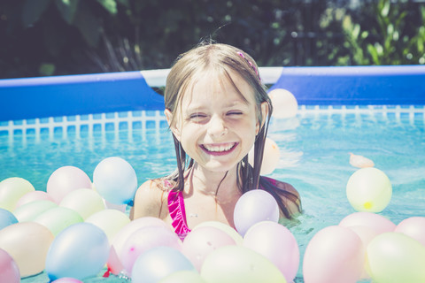 Glückliches Mädchen im Schwimmbad umgeben von Luftballons, lizenzfreies Stockfoto