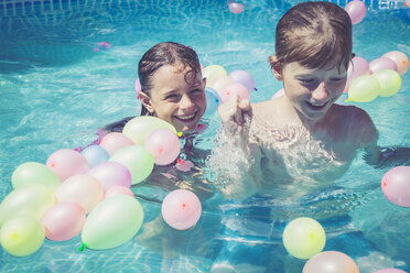 Happy boy and girl in swimming pool surrounded by balloons - SARF002072