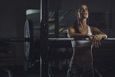 Muskulöser Sportler stützt sich im Fitnessstudio auf eine Langhantel - MADF000460