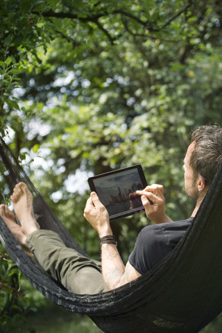 Entspannter Mann in Hängematte liegend mit digitalem Tablet, lizenzfreies Stockfoto