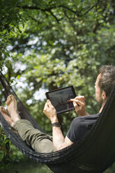 Entspannter Mann in Hängematte liegend mit digitalem Tablet - ONF000829