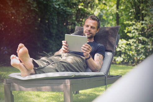 Entspannter Mann liegt im Liegestuhl im Garten und benutzt ein digitales Tablet - ONF000834