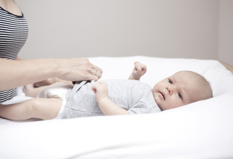 Young woman dressing baby lying on changing table stock photo