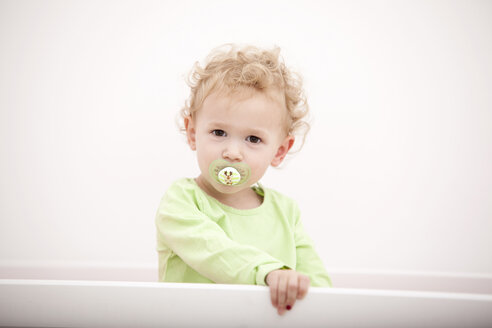Porträt eines kleinen blonden Mädchens mit Schnuller im Kinderbett - MFRF000301