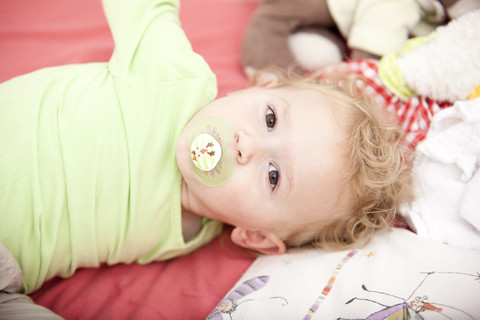 Porträt eines kleinen blonden Mädchens mit Schnuller auf einem Kinderbett liegend, lizenzfreies Stockfoto