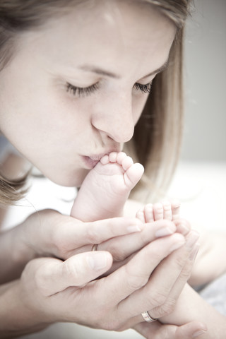 Junge Mutter küsst den Fuß eines kleinen Mädchens, lizenzfreies Stockfoto