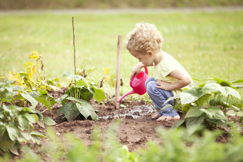 Kleines Mädchen, das im Garten hockt und Pflanzen gießt, lizenzfreies Stockfoto