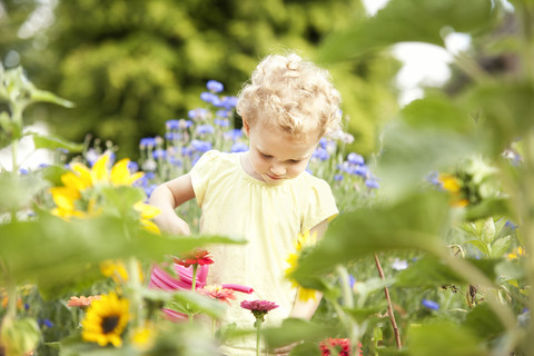 Kleines Mädchen, das im Garten steht und Blumen gießt, lizenzfreies Stockfoto