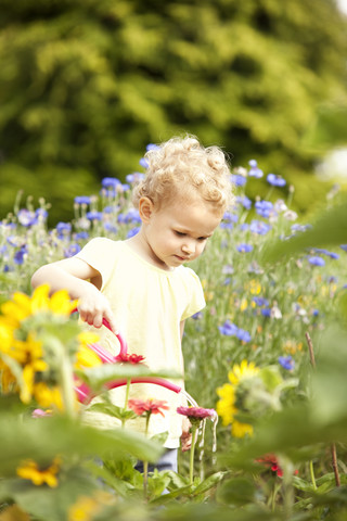 Kleines Mädchen, das im Garten steht und Blumen gießt, lizenzfreies Stockfoto