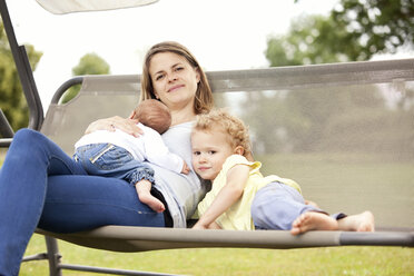 Portrait of happy young mother with her two little daughters on a canopy swing - MFRF000330