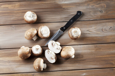 Sliced and whole Crimini Mushrooms and a kitchen knife on wood - CSF025956