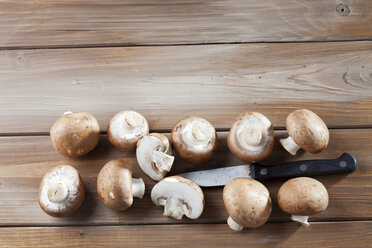 Sliced and whole Crimini Mushrooms and a kitchen knife on wood - CSF025957