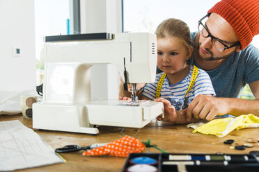 Father and daughter at home using sewing machine - UUF005134