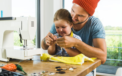 Father and daughter at home using sewing machine - UUF005138