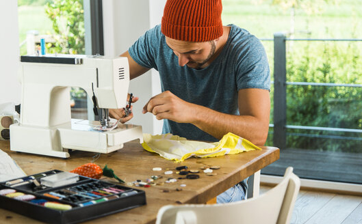 Young man at home using sewing machine - UUF005140