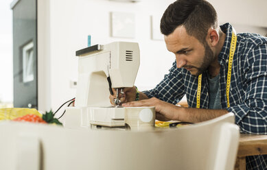 Young man at home using sewing machine - UUF005147