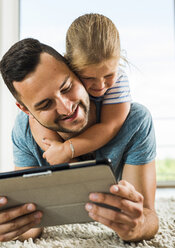 Glücklicher Vater und Tochter auf dem Teppich liegend mit digitalem Tablet - UUF005158
