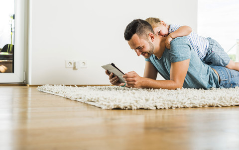 Glücklicher Vater und Tochter auf dem Teppich liegend mit digitalem Tablet, lizenzfreies Stockfoto