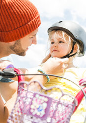 Father closing daughter's helmet on bike - UUF005188