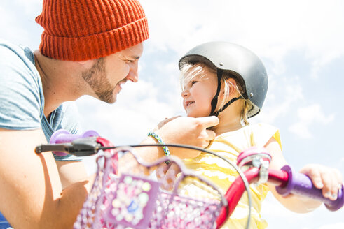 Father closing daughter's helmet on bike - UUF005189