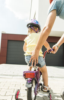 Vater unterstützt Tochter auf dem Fahrrad - UUF005194