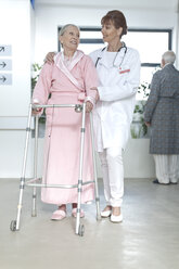 Arzt führt älteren Patienten mit Gehhilfe auf dem Krankenhausboden - ZEF007237