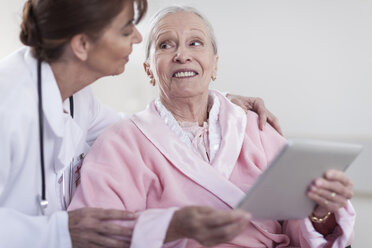 Doctor and smiling elderly patient in wheelchair with digital tablet - ZEF007246