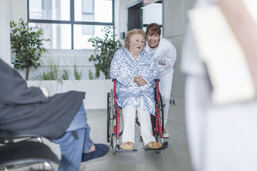 Arzt mit älterem Patienten im Rollstuhl auf dem Krankenhausboden - ZEF007291