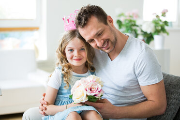 Girl wearing pink crown sitting on father's lap with bunch of flowers - WESTF021483