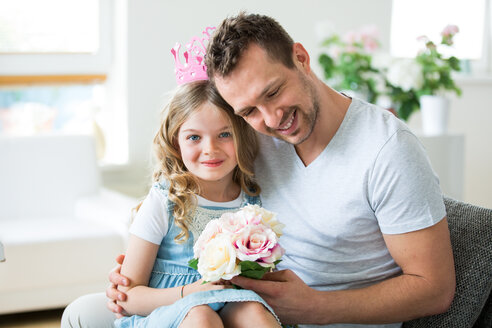 Mädchen mit rosa Krone sitzt auf dem Schoß des Vaters mit Blumenstrauß - WESTF021483