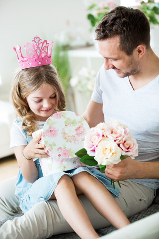 Mädchen mit rosa Krone sitzt auf dem Schoß des Vaters mit Blumenstrauß, lizenzfreies Stockfoto