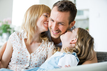 Happy family sitting on couch, mother and daughter kissing father - WESTF021496