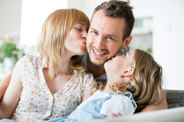 Happy family sitting on couch, mother and daughter kissing father - WESTF021497