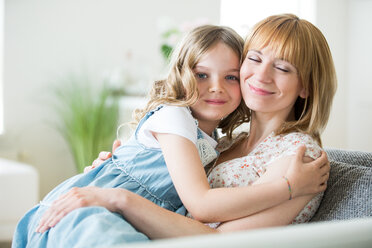 Mother and daughter sitting on couch, cuddling - WESTF021498